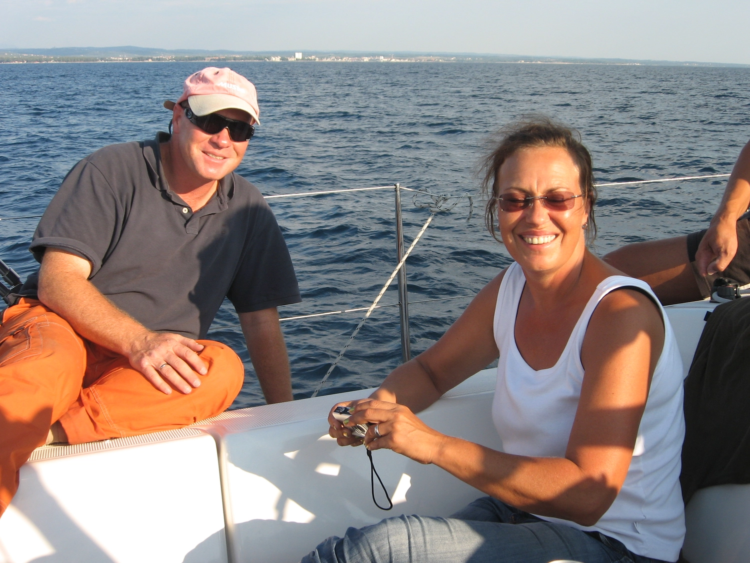 Motorboot-u. Segelschule Ravensburg - Wassersportausbildung und lizenzierung - Ein Mann im Poloshirt und eine Frau im weißen Tanktop lächeln, während sie zusammen auf dem Deck eines Segelboots sitzen.