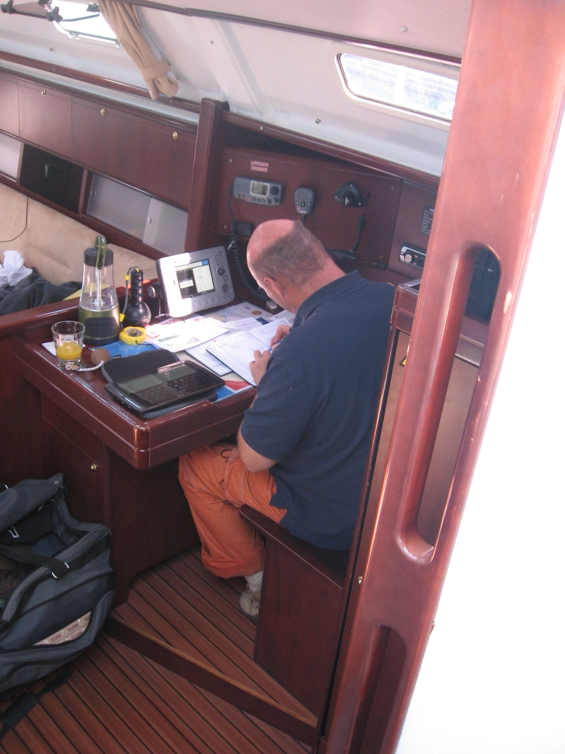 Motorboot-u. Segelschule Ravensburg - Wassersportausbildung und lizenzierung - Ein Mann in blauem Hemd und orangefarbener Hose sitzt an einem kleinen Holzschreibtisch in einer Bootskabine und blättert in Papieren.