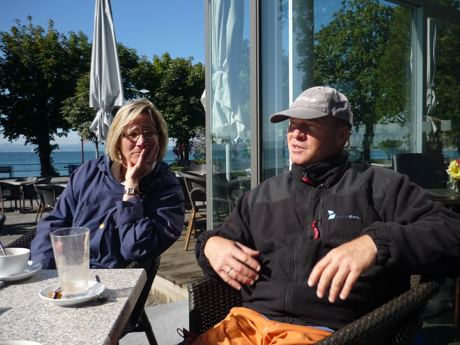 Motorboot-u. Segelschule Ravensburg - Wassersportausbildung und lizenzierung - Eine Frau und ein Mann in Jacken sitzen an einem Tisch in der Nähe eines festgemachten Bootes.