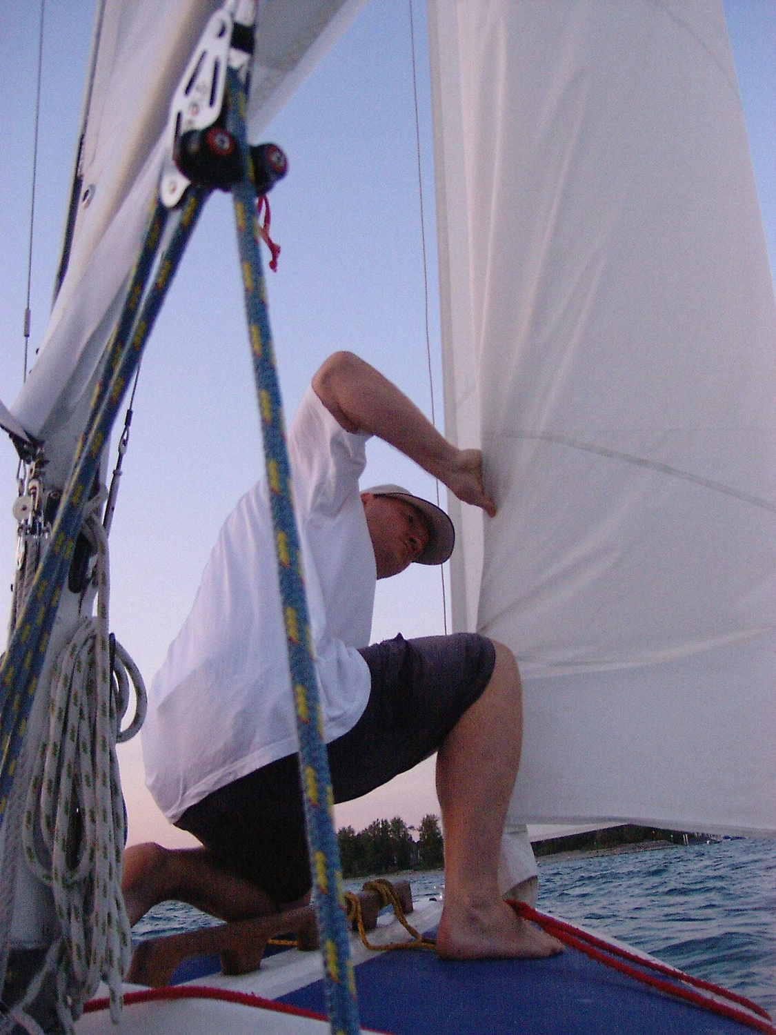 Motorboot-u. Segelschule Ravensburg - Wassersportausbildung und lizenzierung - Eine Person auf einem Boot justiert ein weißes Segel vor blauem Himmel.