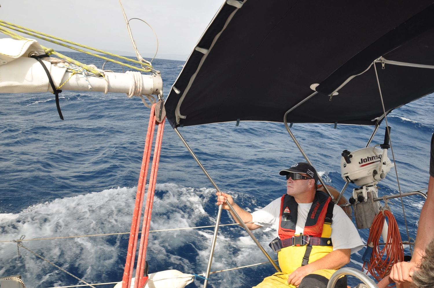 Motorboot-u. Segelschule Ravensburg - Wassersportausbildung und lizenzierung - Ein Mann mit Schwimmweste und Sonnenbrille steuert ein Segelboot über offenes blaues Wasser.