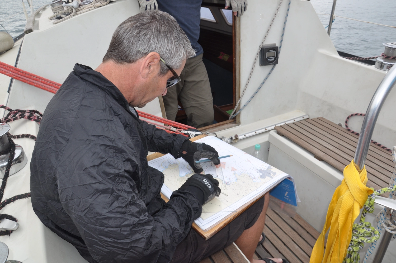 Motorboot-u. Segelschule Ravensburg - Wassersportausbildung und lizenzierung - Ein Mann in einer grauen Jacke sitzt auf einem Boot und ist ganz in das Schreiben oder Zeichnen auf einem Dokument vertieft.