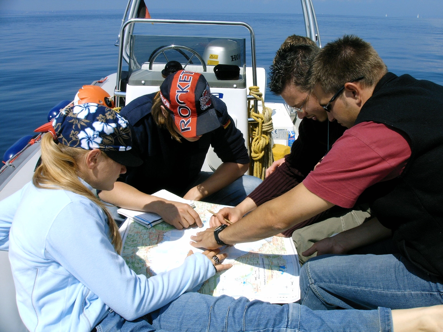 Motorboot-u. Segelschule Ravensburg - Wassersportausbildung und lizenzierung - Drei Personen saßen eng beieinander auf dem Deck eines Bootes und studierten konzentriert eine große Papierkarte.