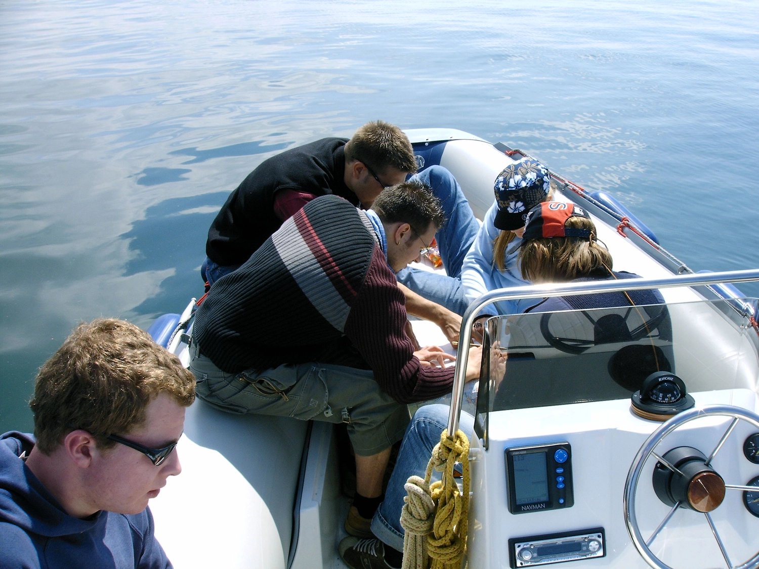 Motorboot-u. Segelschule Ravensburg - Wassersportausbildung und lizenzierung - Mehrere Personen hatten sich auf einem kleinen Motorboot versammelt und blickten auf Ausrüstung oder eine Karte hinunter.