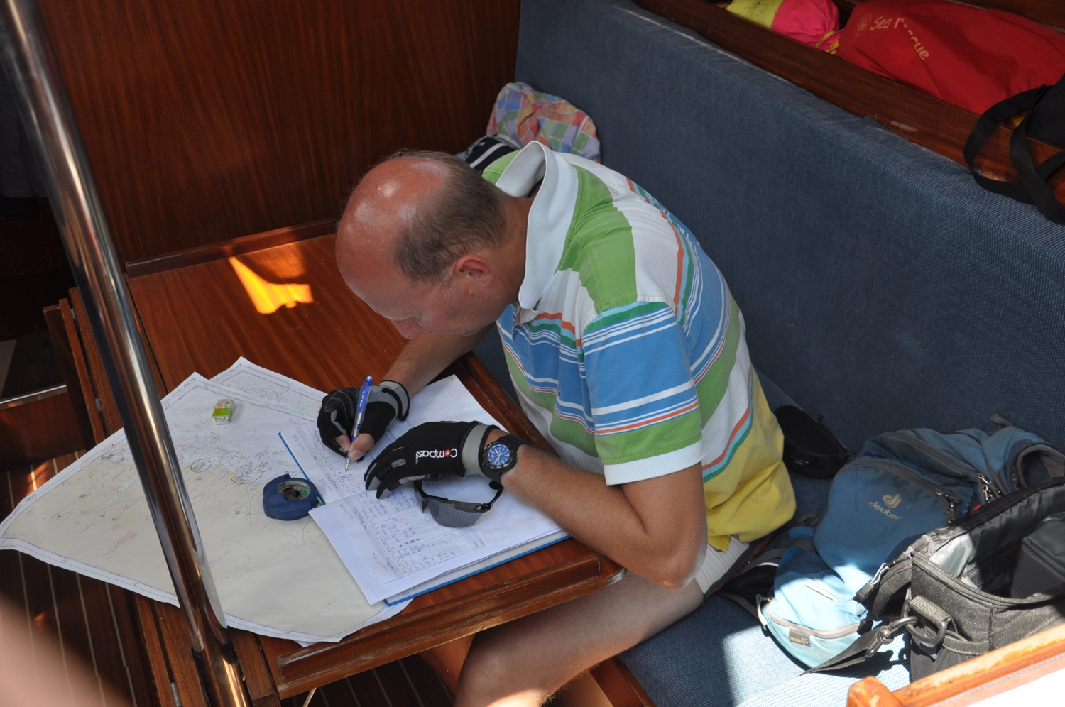 Motorboot-u. Segelschule Ravensburg - Wassersportausbildung und lizenzierung - Ein Mann in einem gestreiften Hemd sitzt an einem kleinen Schreibtisch in einer Bootskabine und schreibt in ein Logbuch.