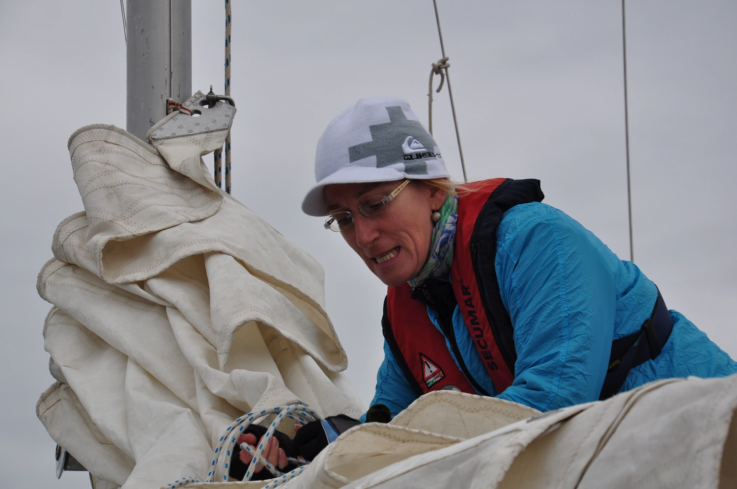 Motorboot-u. Segelschule Ravensburg - Wassersportausbildung und lizenzierung - Ein Mann in blauer Jacke und weißer Mütze arbeitet mit einem großen weißen Segel.