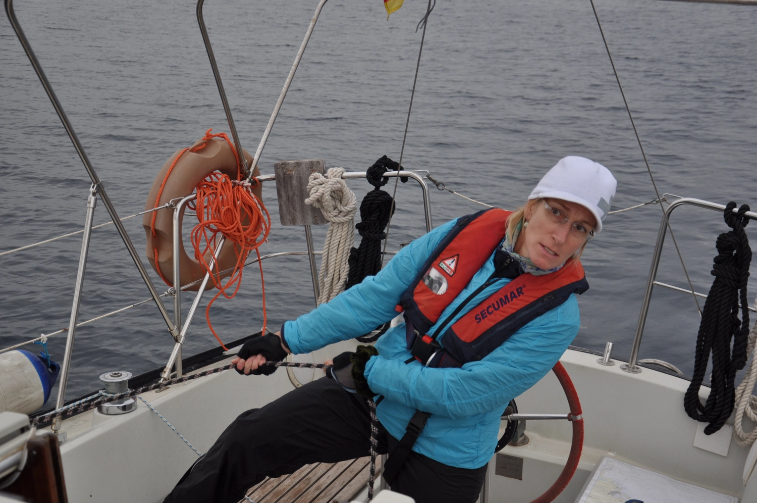 Motorboot-u. Segelschule Ravensburg - Wassersportausbildung und lizenzierung - Eine Person in blauer Jacke und Schwimmweste bedient die Pinne eines Segelboots.