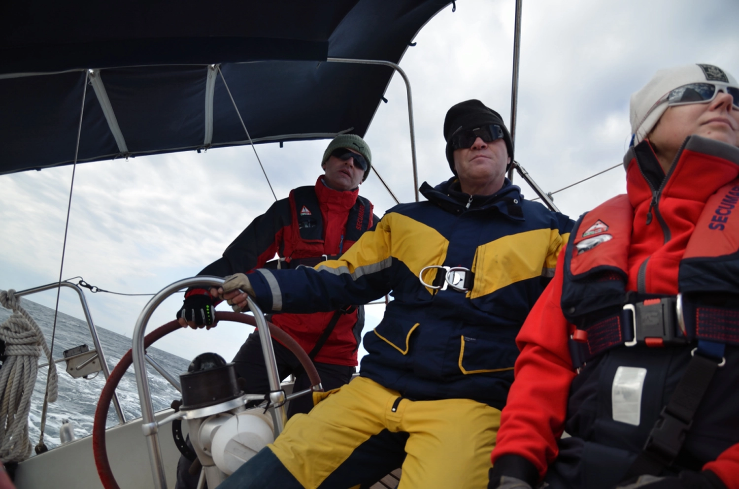 Motorboot-u. Segelschule Ravensburg - Wassersportausbildung und lizenzierung - Eine Gruppe von Menschen in schwerer Segelausrüstung und Schwimmwesten posiert auf dem Deck eines Bootes.
