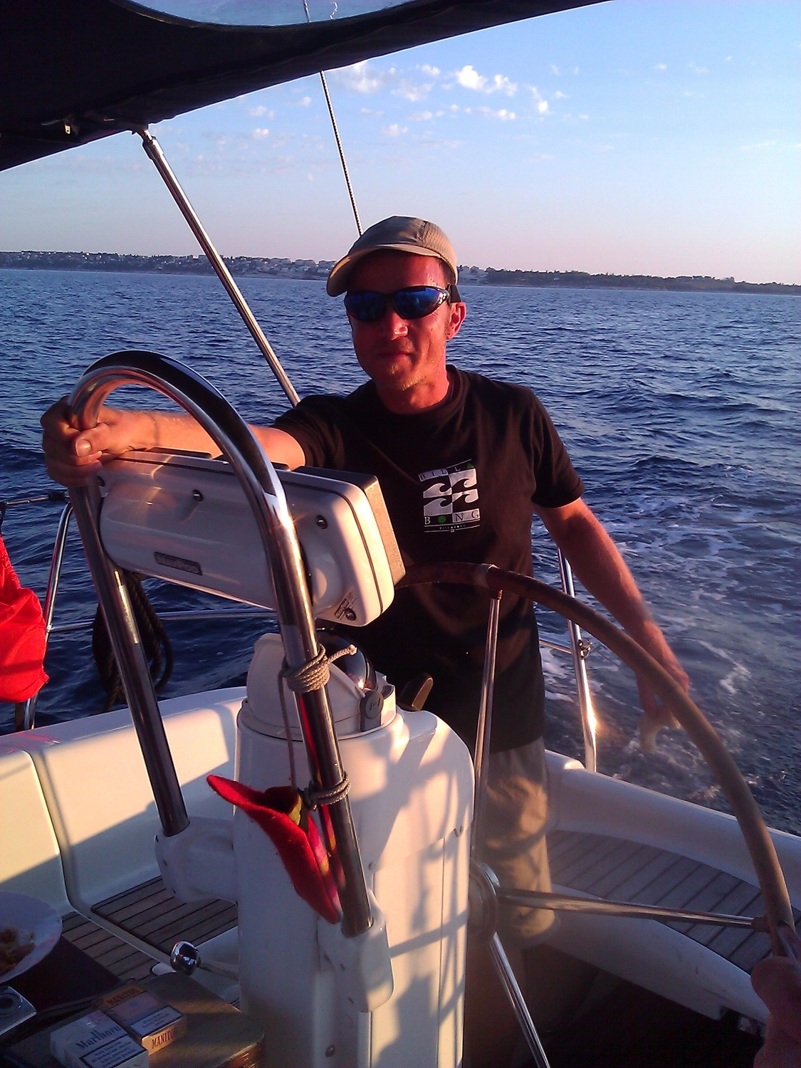 Motorboot-u. Segelschule Ravensburg - Wassersportausbildung und lizenzierung - Ein Mann mit Sonnenbrille und schwarzem T-Shirt steuert ein Segelboot.