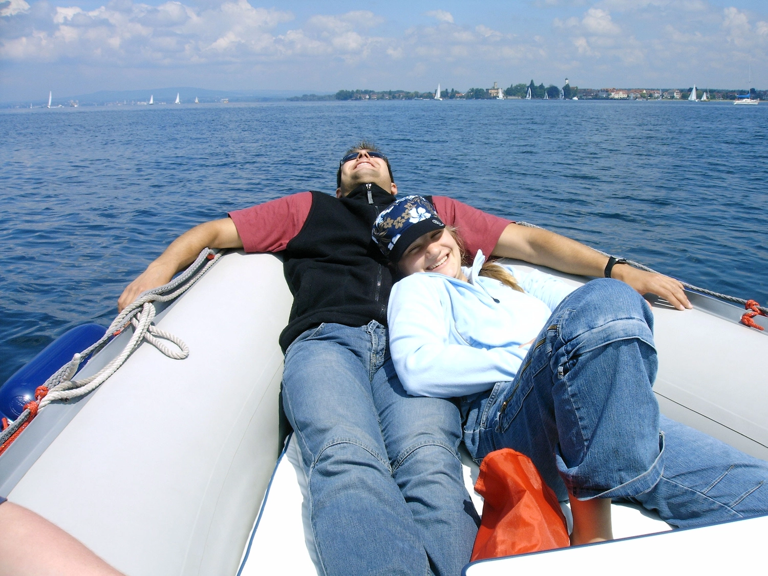 Motorboot-u. Segelschule Ravensburg - Wassersportausbildung und lizenzierung - Ein Paar entspannt sich und sonnt sich auf dem Bug eines weißen Bootes auf dem Wasser.