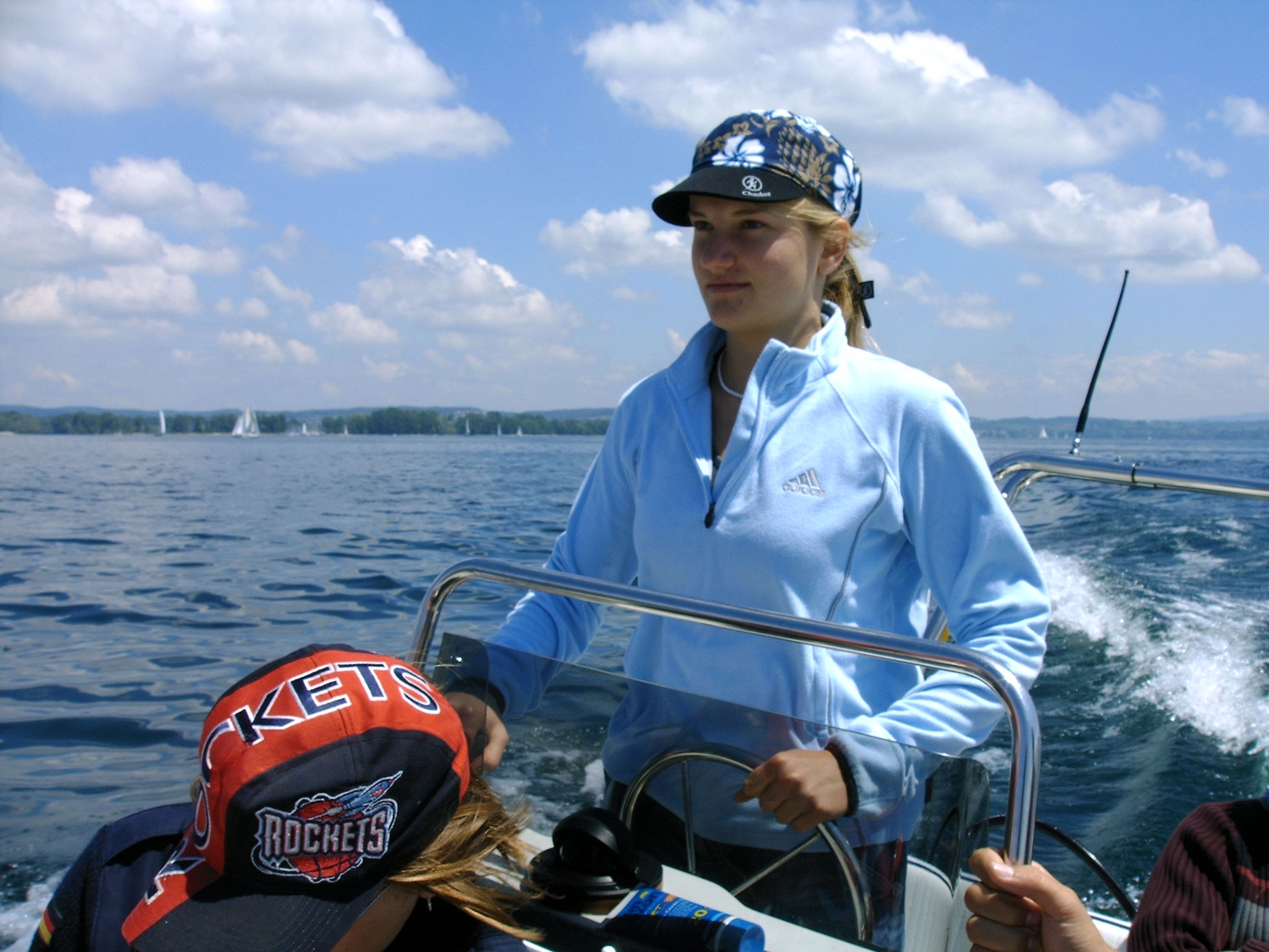 Motorboot-u. Segelschule Ravensburg - Wassersportausbildung und lizenzierung - Eine junge Frau in einer blauen Jacke lächelt, während sie am Steuer eines Bootes steht.