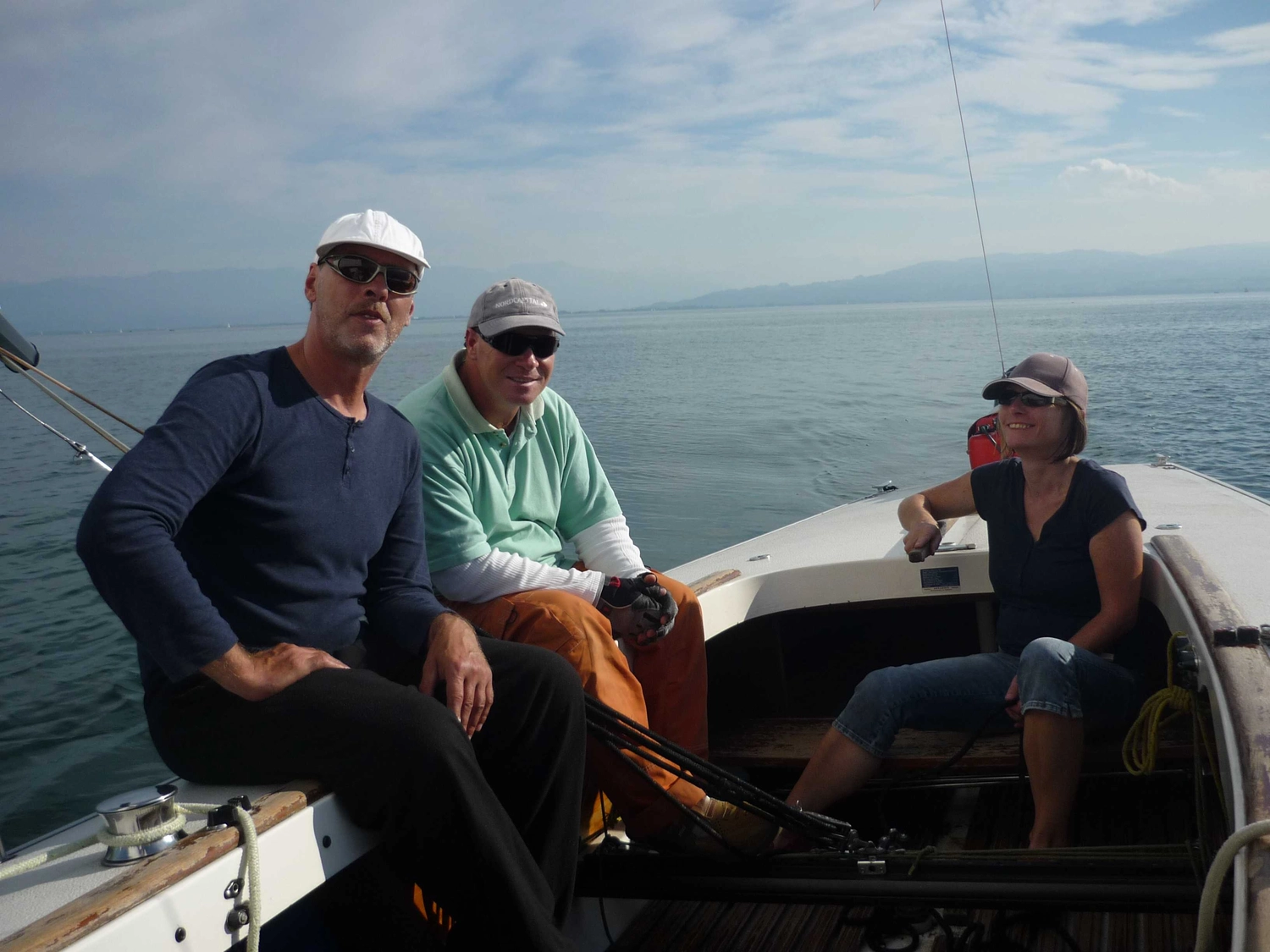 Motorboot-u. Segelschule Ravensburg - Wassersportausbildung und lizenzierung - Drei Personen mit Hüten und in Freizeitkleidung sitzen auf einem Segelboot und genießen einen klaren Tag auf dem offenen Wasser.