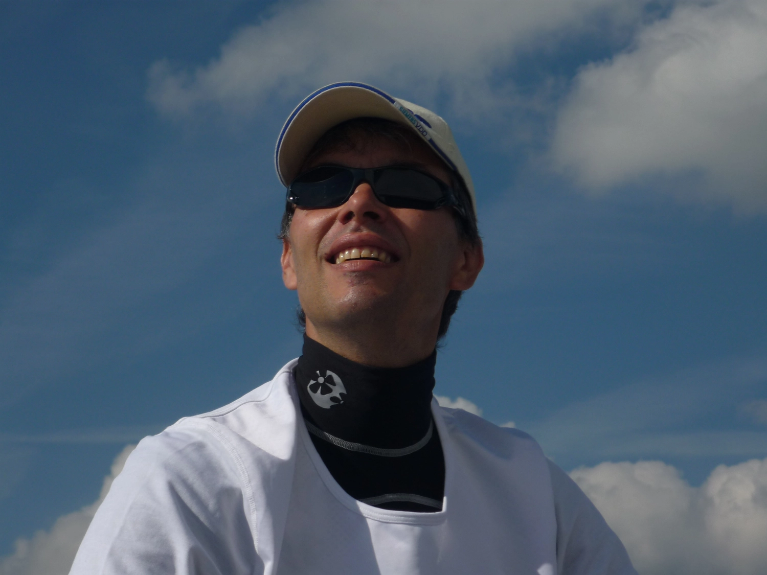 Motorboot-u. Segelschule Ravensburg - Wassersportausbildung und lizenzierung - Eine Nahaufnahme aus der Froschperspektive zeigt einen lächelnden Mann mit Sonnenbrille und weißem Hemd vor blauem Himmel.