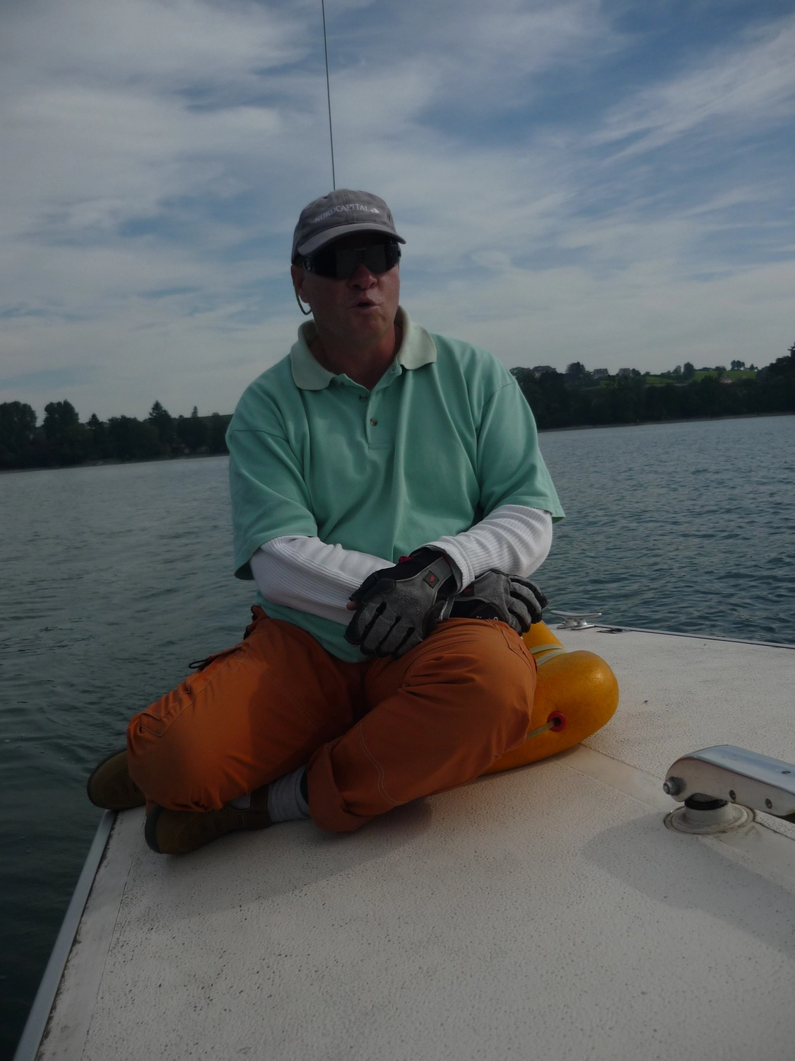 Motorboot-u. Segelschule Ravensburg - Wassersportausbildung und lizenzierung - Ein Mann in einem hellgrünen Polohemd und orangefarbenen Hosen sitzt am Rand eines Bootes auf ruhigem Wasser.