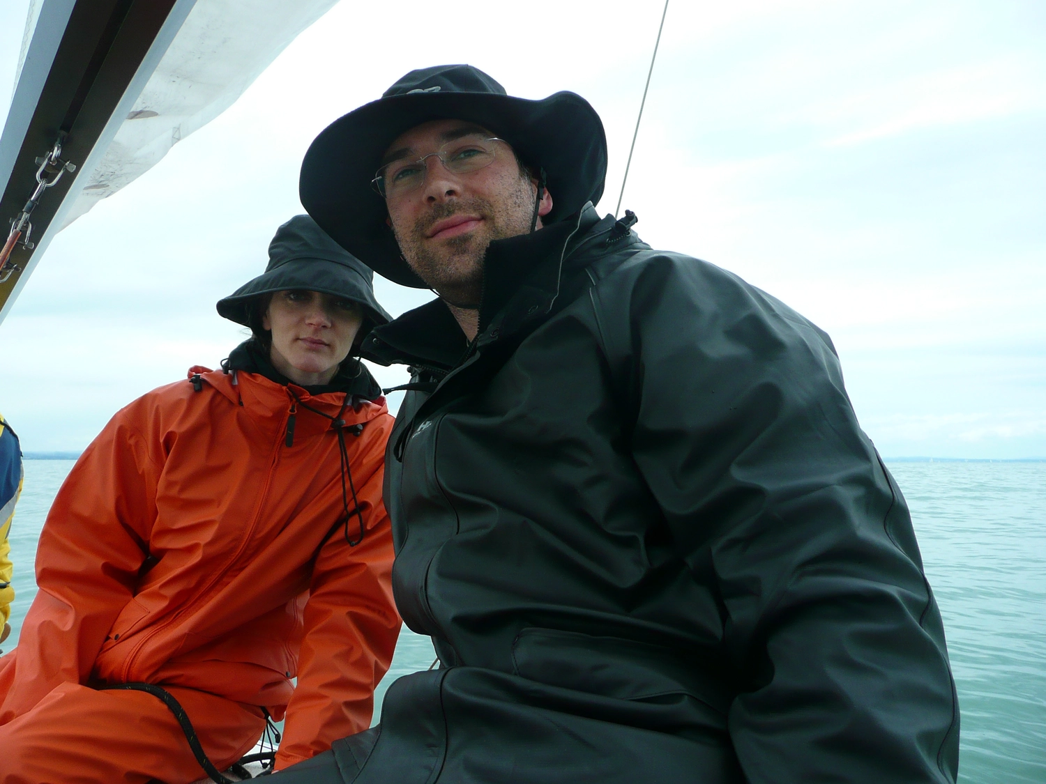 Motorboot-u. Segelschule Ravensburg - Wassersportausbildung und lizenzierung - Zwei Personen auf einem Boot, die schwere Segeljacken tragen; der Mann im Vordergrund trägt einen schwarzen Hut mit breiter Krempe.