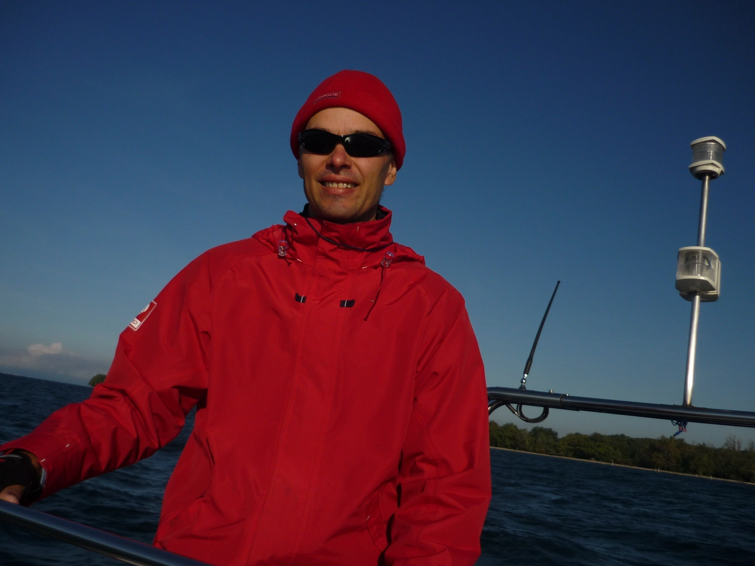 Motorboot-u. Segelschule Ravensburg - Wassersportausbildung und lizenzierung - Ein Mann mit einer leuchtend roten Jacke, Sonnenbrille und roter Mütze steht auf einem Boot.
