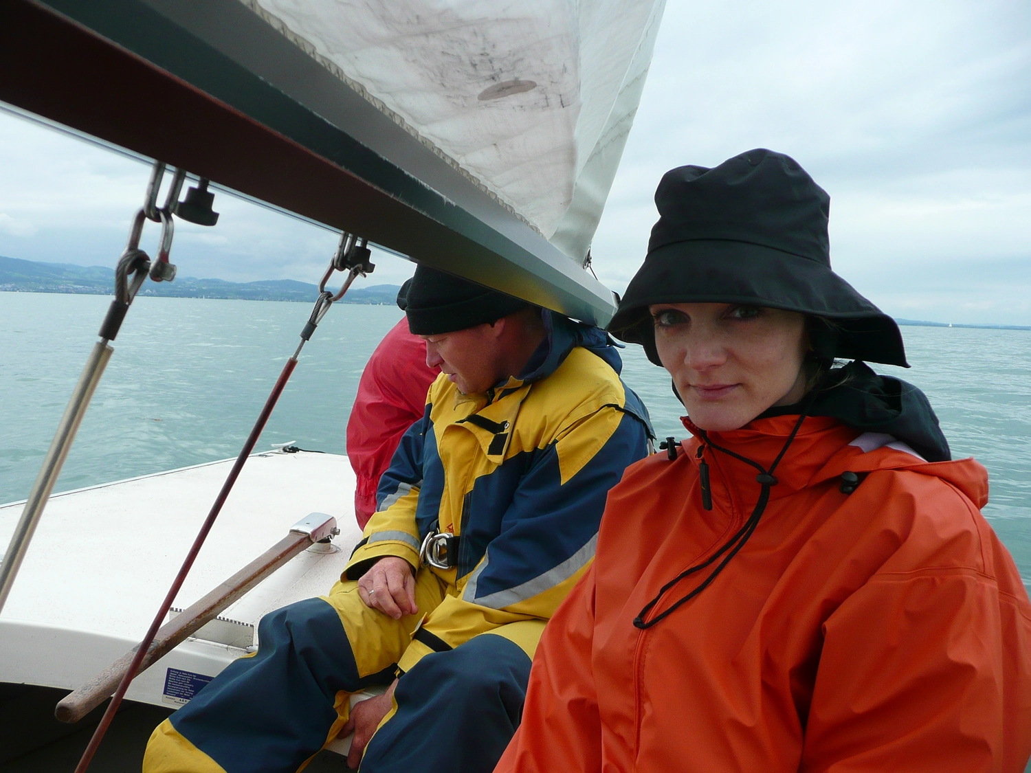 Motorboot-u. Segelschule Ravensburg - Wassersportausbildung und lizenzierung - Zwei Personen in auffälliger Regenkleidung segeln; eine in Gelb und eine in Orange mit schwarzem Sonnenhut.