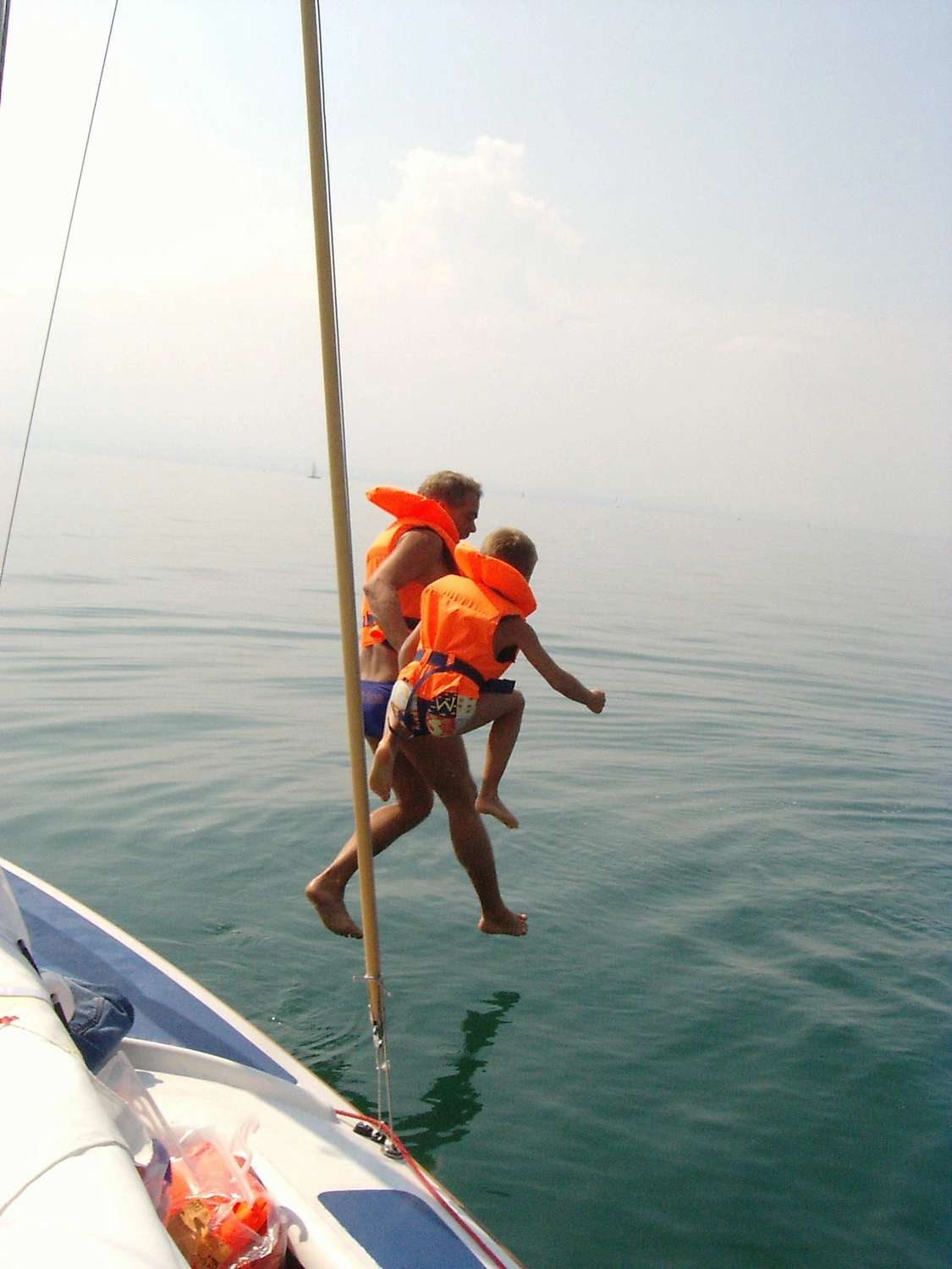 Motorboot-u. Segelschule Ravensburg - Wassersportausbildung und lizenzierung - Ein Mann und ein kleines Kind in orangefarbenen Schwimmwesten springen von einem Boot ins Wasser.