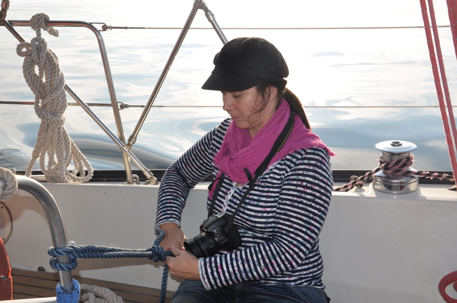 Motorboot-u. Segelschule Ravensburg - Wassersportausbildung und lizenzierung - Eine Frau in einem gestreiften Hemd und einem rosa Schal, die auf einem Segelboot ein Seil handhabt.
