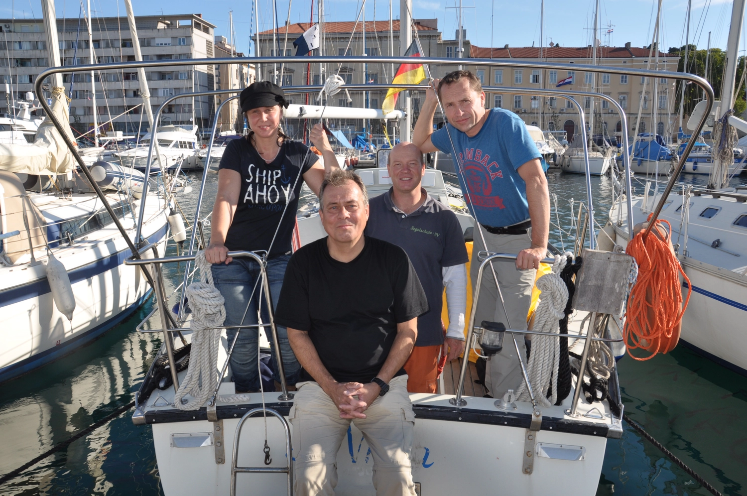 Motorboot-u. Segelschule Ravensburg - Wassersportausbildung und lizenzierung - Eine Gruppe von fünf Personen posiert für ein Foto an Deck eines in einem Yachthafen vor Anker liegenden Bootes.