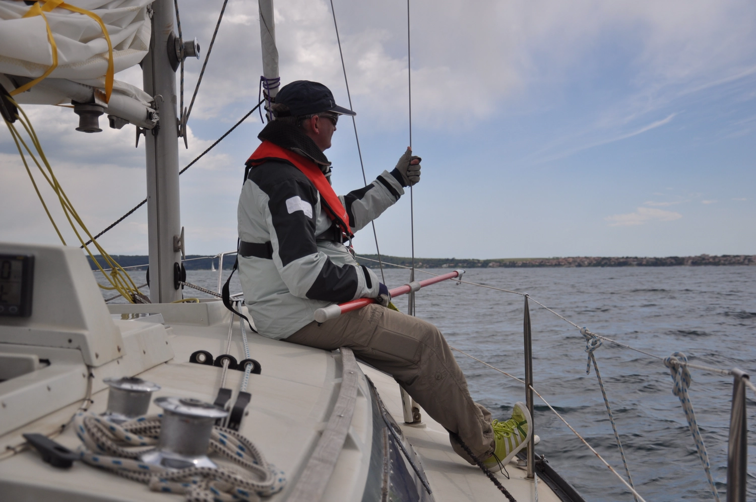 Motorboot-u. Segelschule Ravensburg - Wassersportausbildung und lizenzierung - Eine Person sitzt am Rand eines Segelboots auf offener See und symbolisiert damit einen weltweiten Segel- und Motorbootführerscheinkurs.