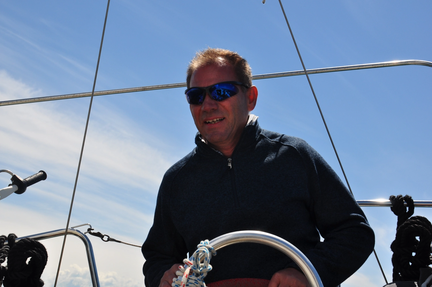 Motorboot-u. Segelschule Ravensburg - Wassersportausbildung und lizenzierung - Ein Mann mit Sonnenbrille lächelt, während er am Steuerrad des Schiffes steht.