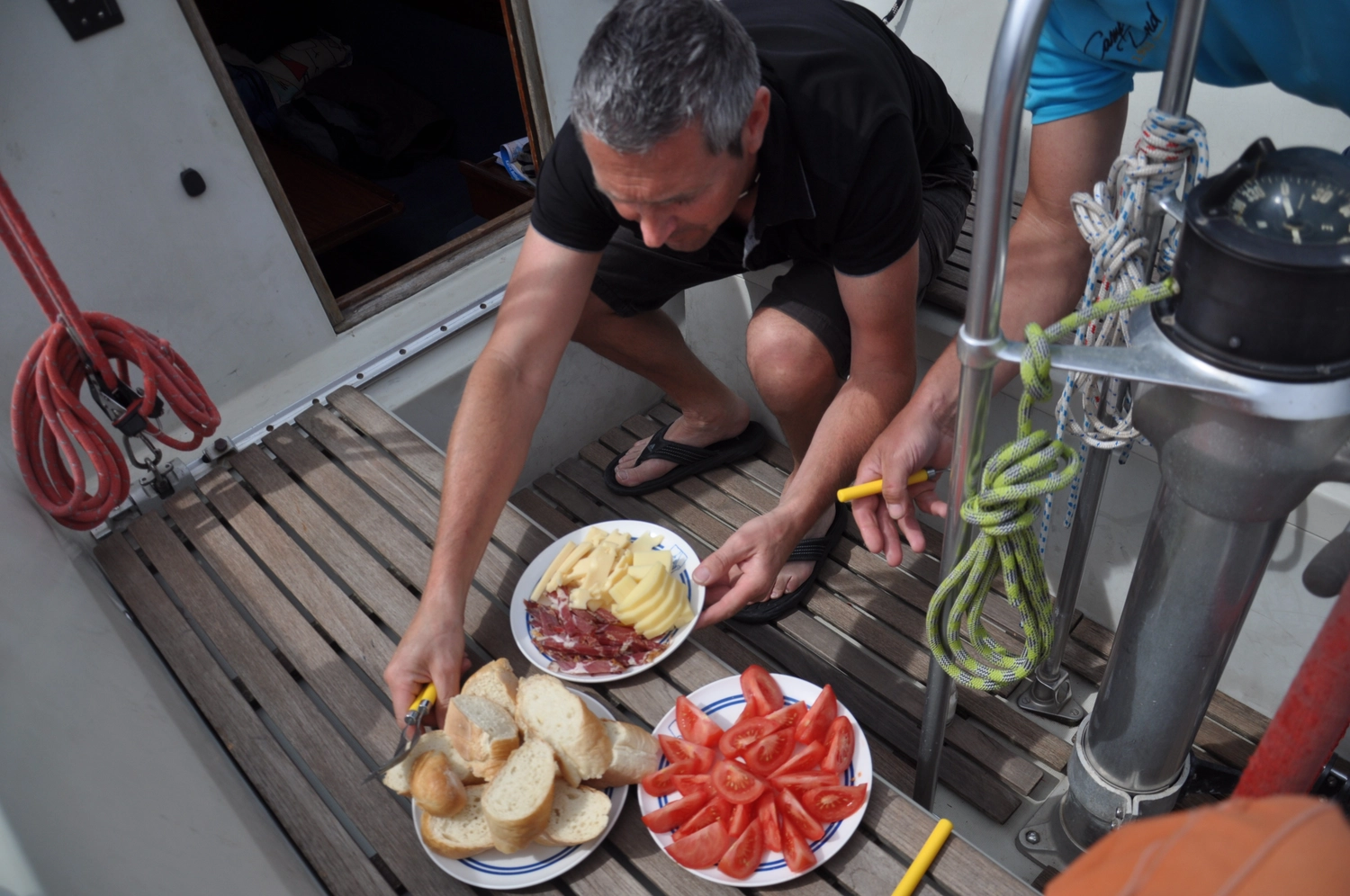 Motorboot-u. Segelschule Ravensburg - Wassersportausbildung und lizenzierung - Männer an Deck bereiten eine Mahlzeit aus Brot, Tomaten und anderen Snacks zu.