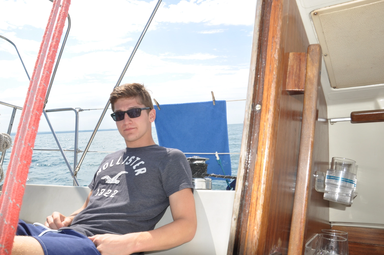 Motorboot-u. Segelschule Ravensburg - Wassersportausbildung und lizenzierung - Ein junger Mann mit Sonnenbrille entspannt auf dem Deck vor blauem Hintergrund.