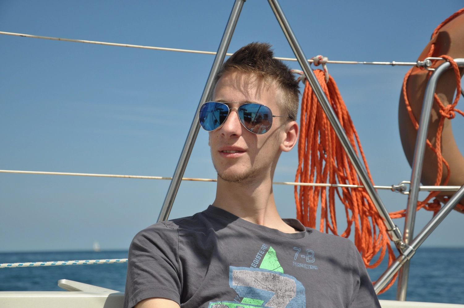 Motorboot-u. Segelschule Ravensburg - Wassersportausbildung und lizenzierung - Nahaufnahme eines jungen Mannes mit Sonnenbrille; hinter ihm ist orangefarbenes Stahlseilwerk zu sehen.