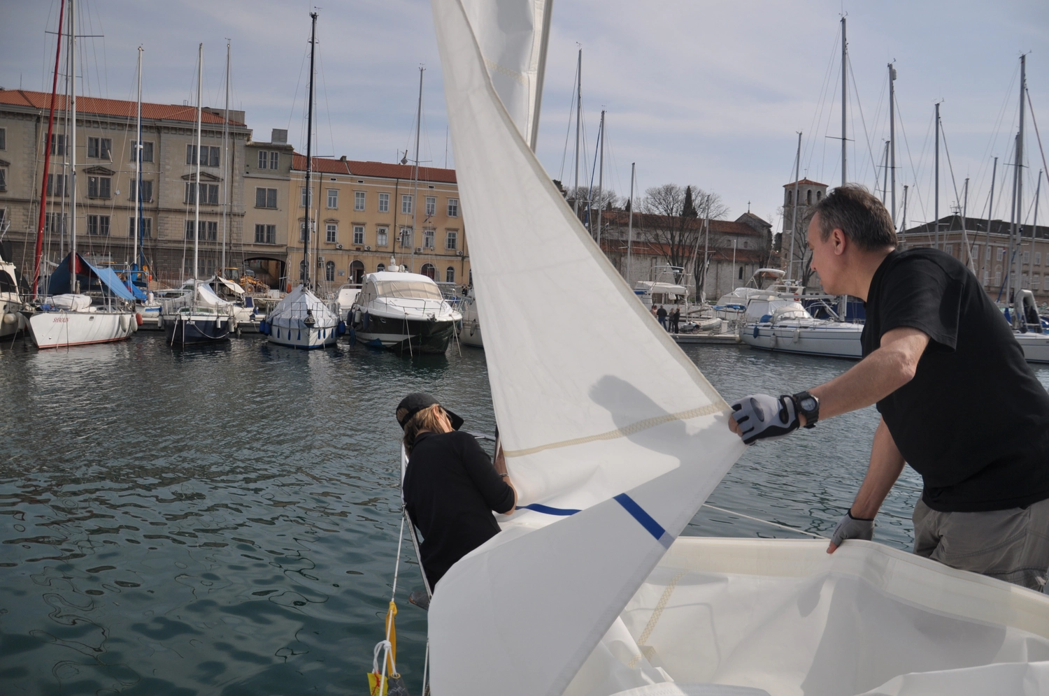 Motorboot-u. Segelschule Ravensburg - Wassersportausbildung und lizenzierung - Ein Besatzungsmitglied arbeitet mit einem weißen Segel auf einem Boot in einem belebten Hafen.