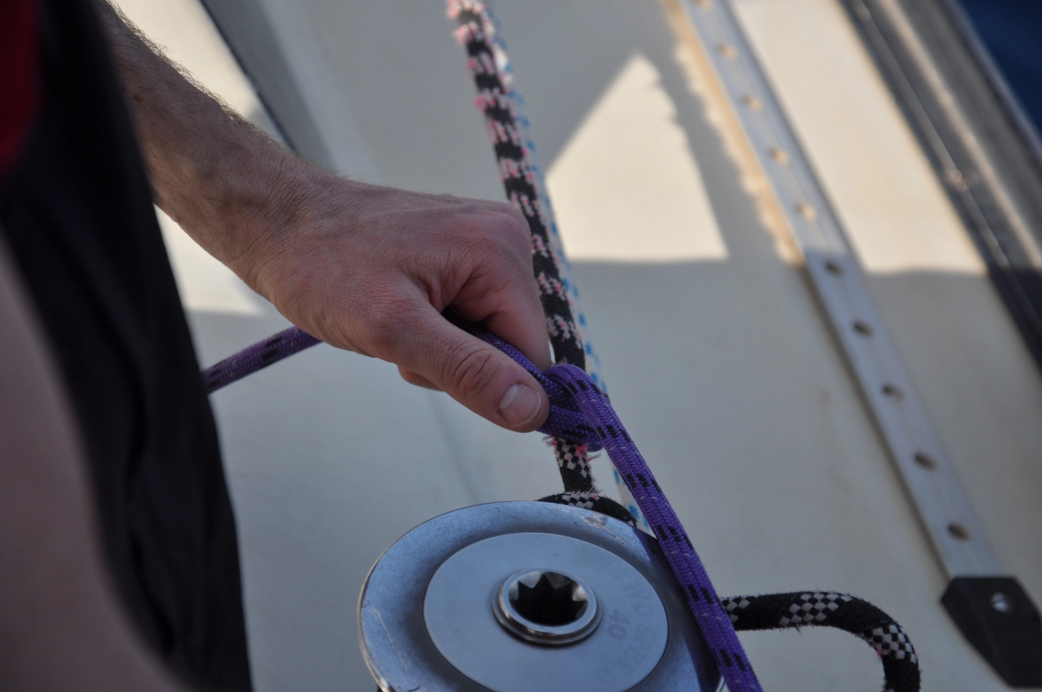 Motorboot-u. Segelschule Ravensburg - Wassersportausbildung und lizenzierung - Nahaufnahme von Händen, die mit violettem Takelwerk und Segelbeschlägen arbeiten.