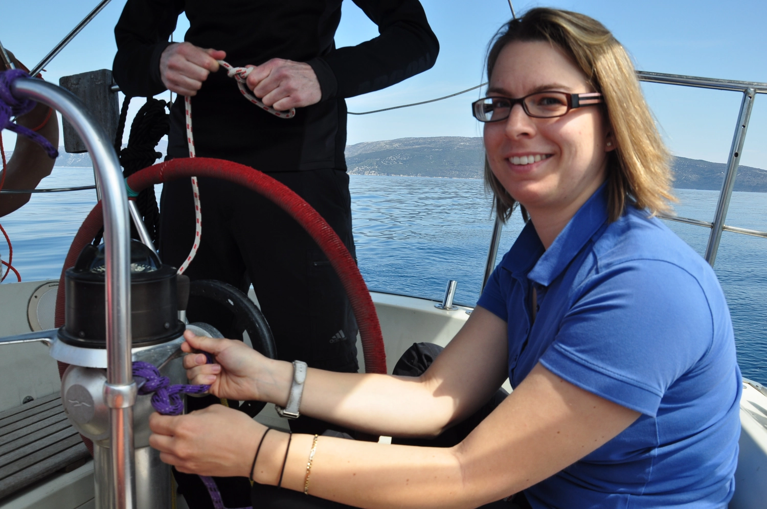 Motorboot-u. Segelschule Ravensburg - Wassersportausbildung und lizenzierung - Eine Frau in einem blauen Poloshirt lächelt, während sie am Steuer eines Segelboots sitzt.
