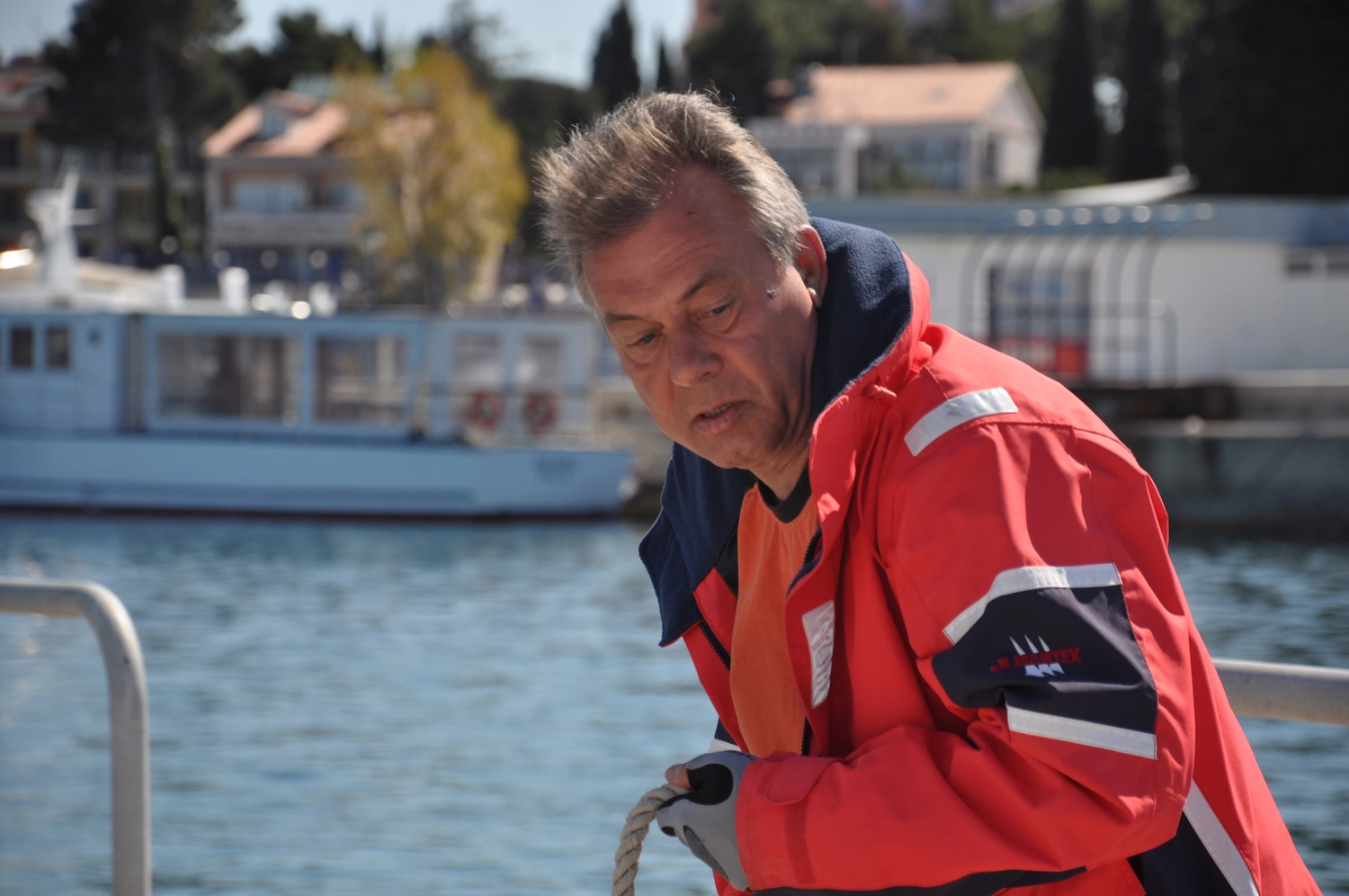 Motorboot-u. Segelschule Ravensburg - Wassersportausbildung und lizenzierung - Nahaufnahme eines Mannes in einer rot-blauen Jacke, der auf einem Boot nach unten schaut.