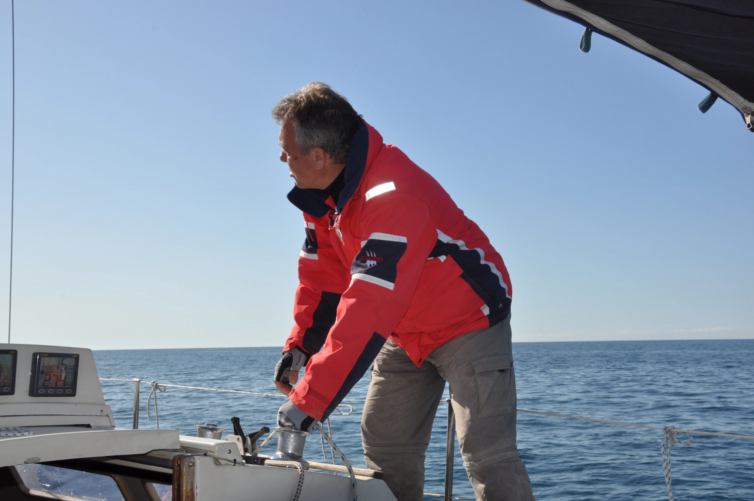Motorboot-u. Segelschule Ravensburg - Wassersportausbildung und lizenzierung - Ein Mann in einer leuchtend roten Segeljacke arbeitet an Deck eines Bootes auf See.