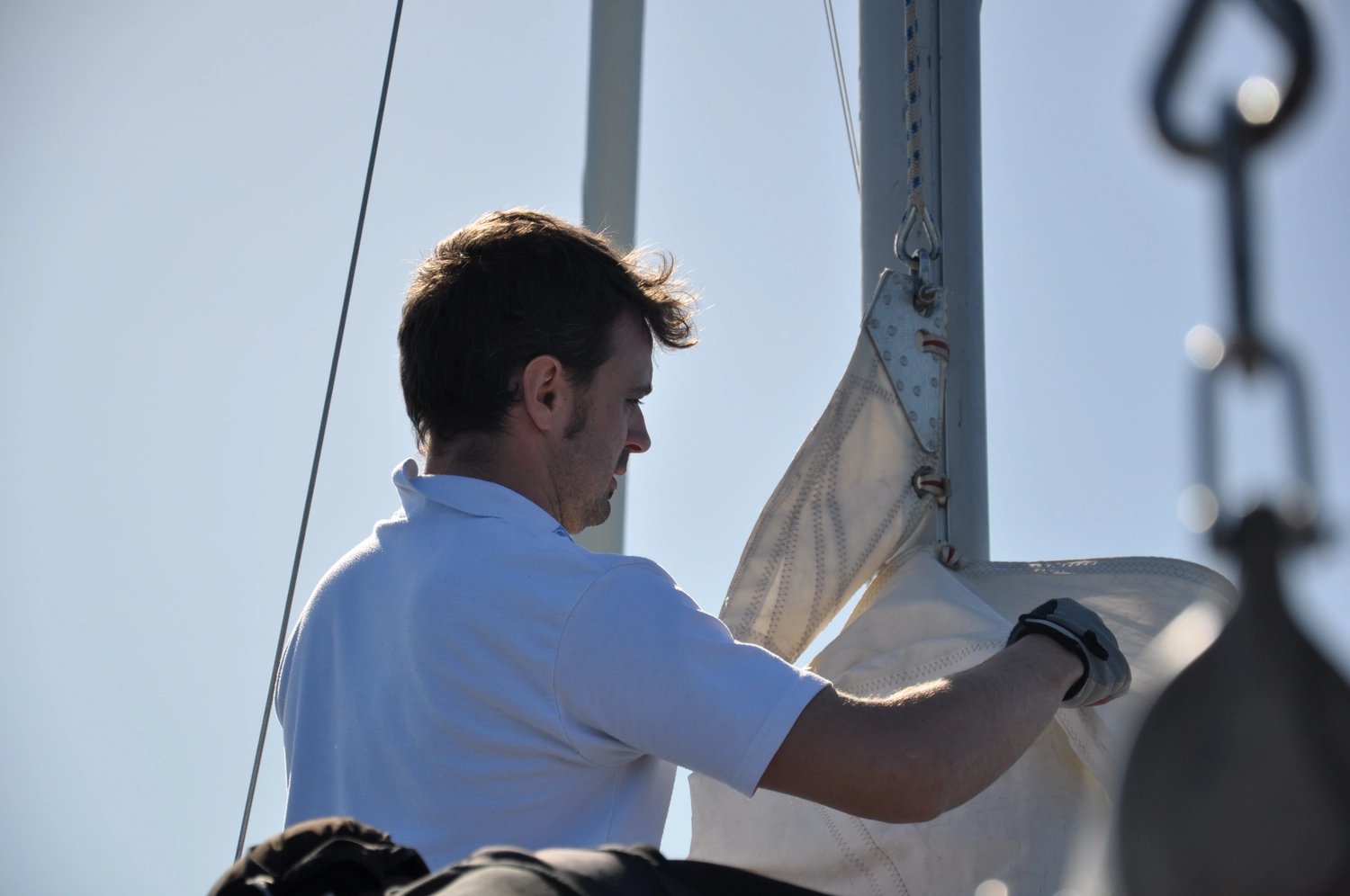 Motorboot-u. Segelschule Ravensburg - Wassersportausbildung und lizenzierung - Seitenprofil eines Mannes in weißem Hemd, der an Deck mit Takelagearbeiten beschäftigt ist.