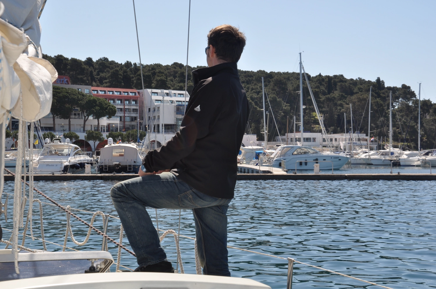 Motorboot-u. Segelschule Ravensburg - Wassersportausbildung und lizenzierung - Ein Mann in einer schwarzen Jacke steht auf einem Boot und blickt auf einen Hafen hinaus.